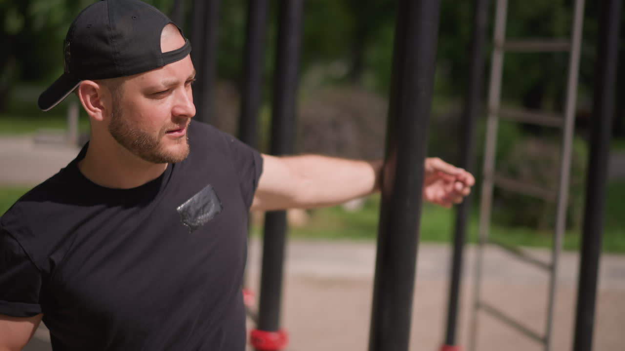 Man In Cap Preparing Muscles Outdoors, Sunlit Park Setting With Man Exercising And Stretching Shoulders, Individual Wearing Black Cap Doing Shoulder Rotations In Bright Outdoor Park Before Training