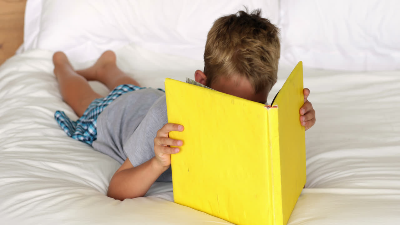 Niño pequeño leyendo un libro amarillo en la cama