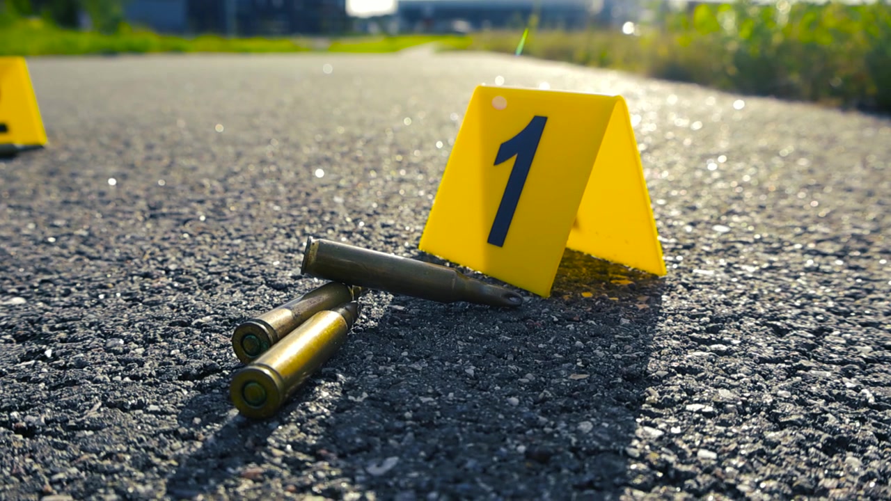 Segnalatori forensi gialli che numerano i bossoli trovati sulla strada asfaltata sulla scena del crimine, suggerendo una recente sparatoria e un'indagine di polizia in corso su un crimine violento