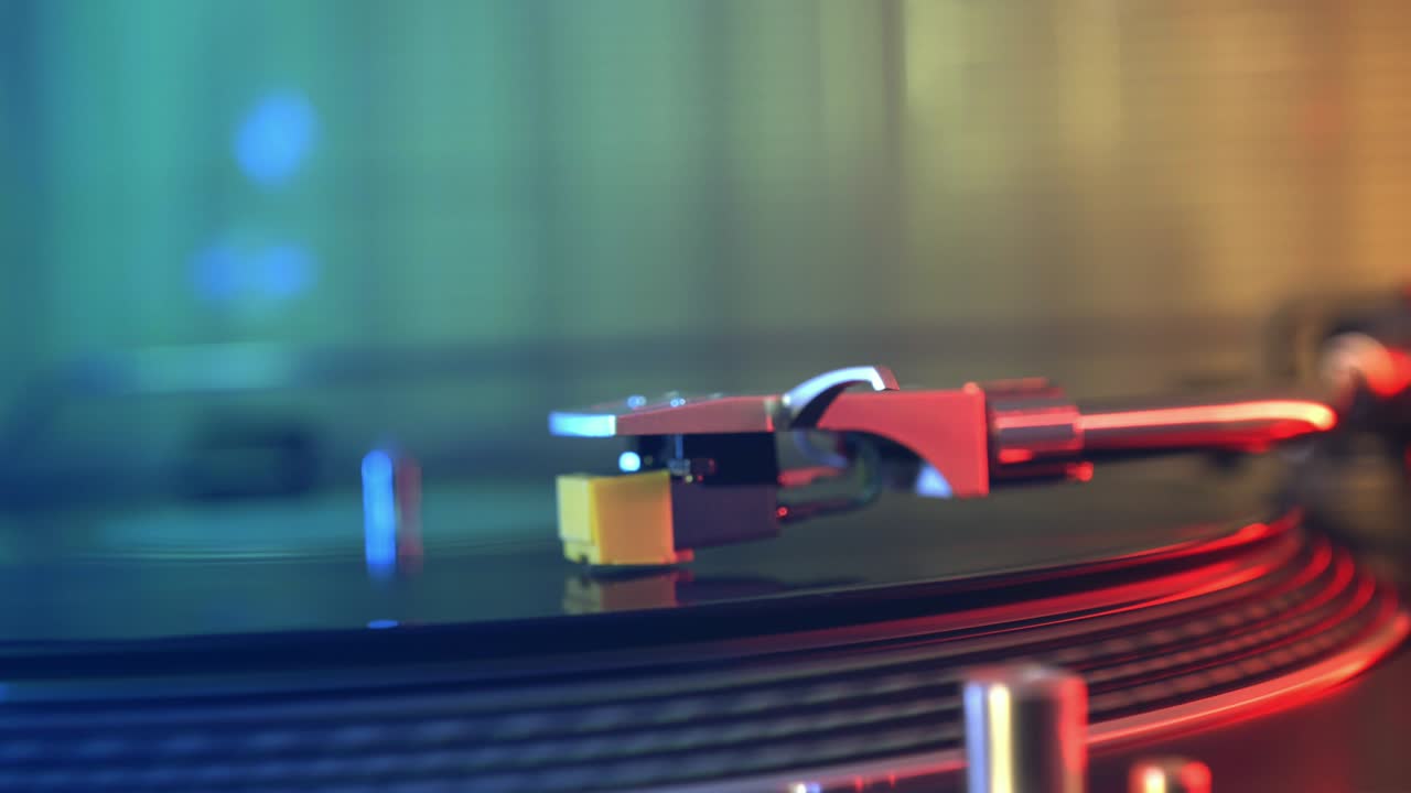 비닐 플레이어 턴테이블: 회전하는 비닐 레코드의 조각, 바늘을 클로즈업으로 가진 스타일러스, 바늘과 비닐 판을 멈추는, 매크로, 전면 뷰, 빨간색과 파란색 빛의 배경에서 흐릿한.