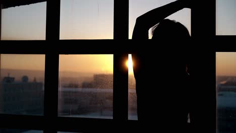 Silhouette-Einer-Frau,-Die-Am-Fenster-Gegen-Sonnenuntergang-Tanzt