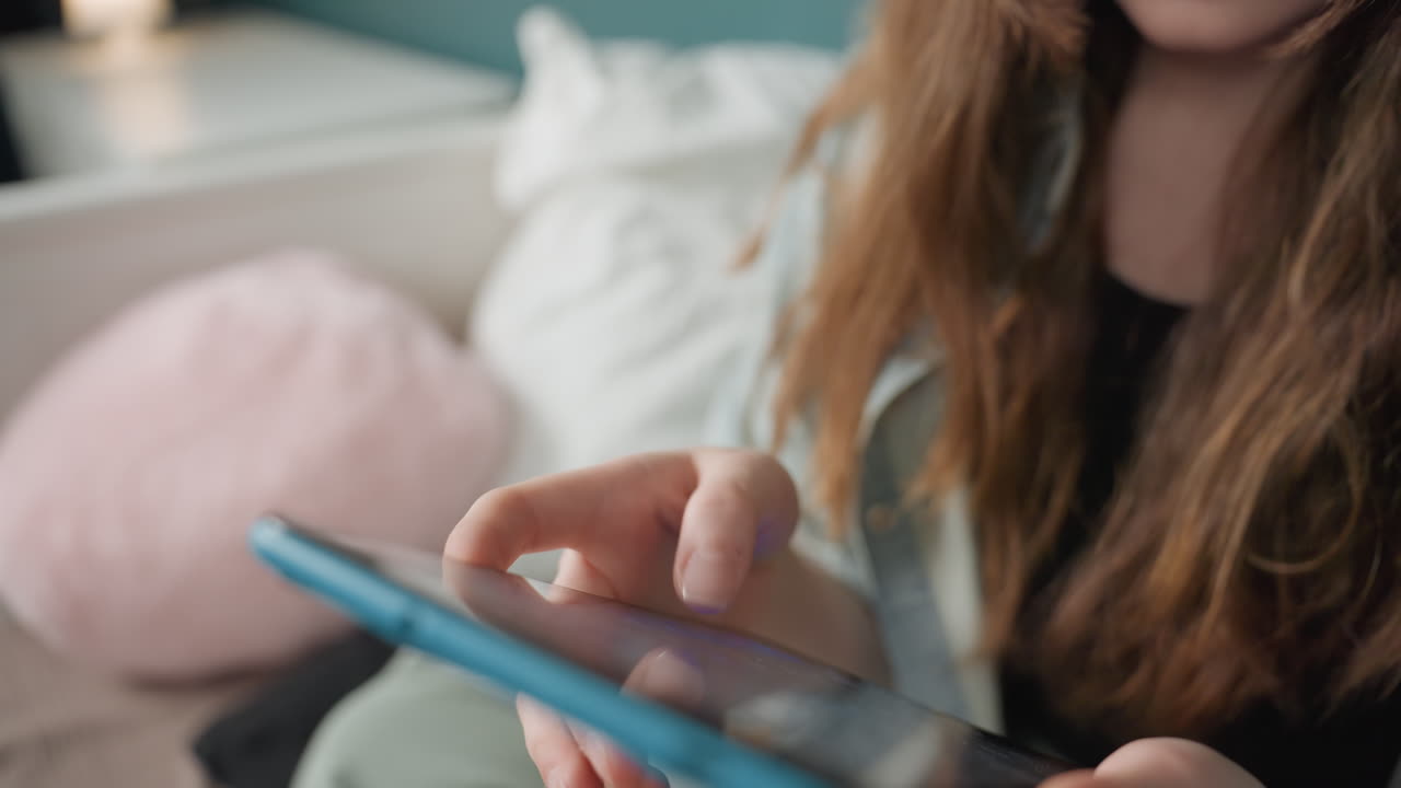 Caucasian girl tapping tablet screen with focused fingers, quick scrolling through messages and app interfaces, notification glow on glass, bedside cushion and soft lamp, social messaging moment
