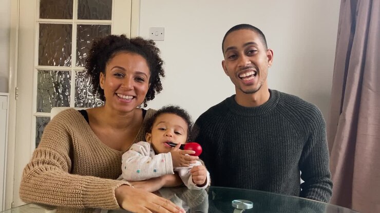 Young Parents with Small Child On Video Call Listening to a Friends Story Directly into Camera