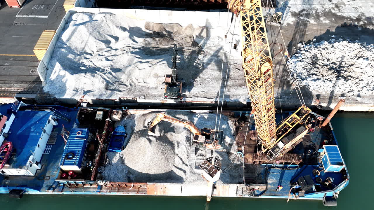 Aerial view of a construction crane at a busy industrial port, sunny day