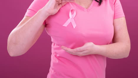 video of midsection of caucasian woman wearing pink cancer awareness ribbon, with pink background