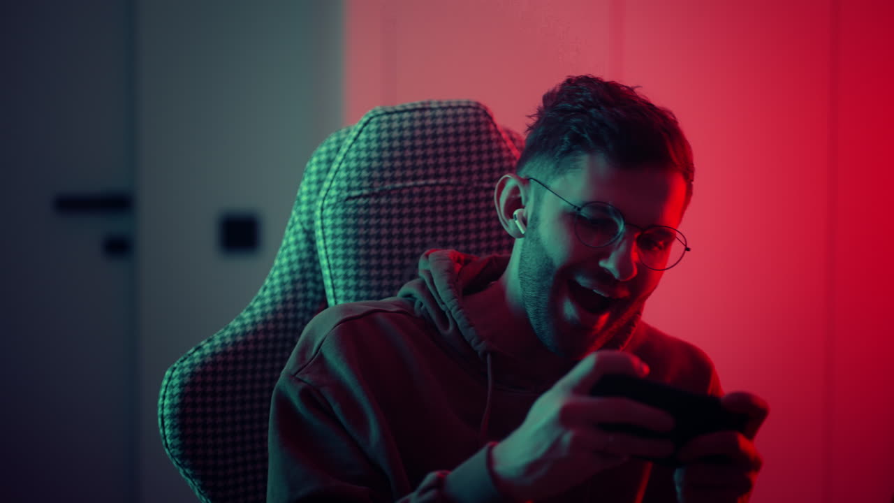 feliz jugador usar auriculares competición jugar videojuego en línea con teléfono inteligente coloridas luces de neón en la sala de estar en casa. esport juego de transmisión en línea casa concepto de actividad de cuarentena. imágenes de alta calidad 4k