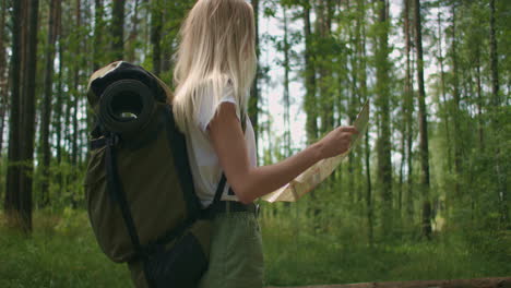 a young woman with a map is walking through the forest traveling with a backpack in slow motion. traveler in shorts in the woods