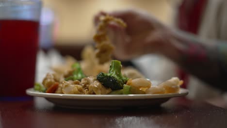 Tätowierter-Bewaffneter-Mann,-Der-Brokkoli,-Hühnchen-Und-Garnelen-Mit-Stäbchen-Im-Chinesischen-Buffett-Restaurant-Drinnen-Isst,-Nachdem-Die-Sperrbeschränkungen-Von-Covid-19-Aufgehoben-Wurden,-In-4k-60fps-Echtzeit