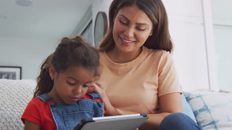 Madre-Hispana-Ayudando-A-Su-Hija-A-Ir-A-La-Escuela-En-Casa-Y-Hacer-La-Tarea-Con-Una-Tableta-Digital