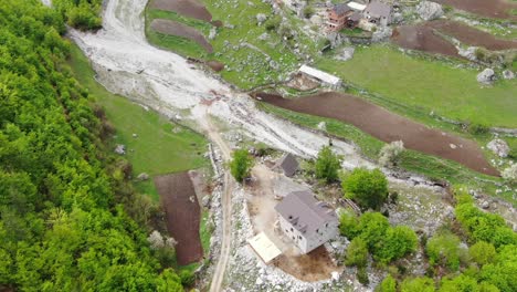 drone view in albania flying over green landscape in a valley surrouned by mountains and small houses with white roads