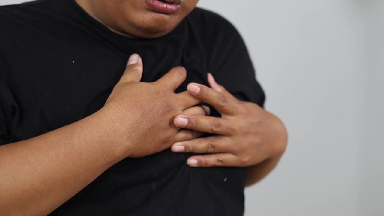 Close up of Asian overweight man's hand holding his chest, having chest pains, suffering from heart pressure indoors