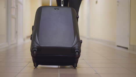 woman carries big black suitcase on tile floor of corridor