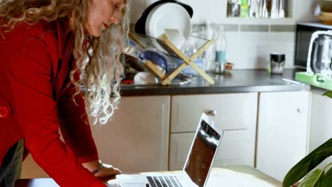 Mature-woman-writing-on-notepad-in-kitchen-4k