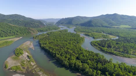 aerial view of a winding river flowing through a green forest with mountains in the background