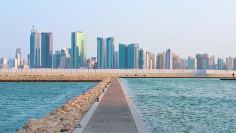 soft wind blowing blue sea waves on the shore, walkway cement and rock shore with modern buildings of manama, bahrain