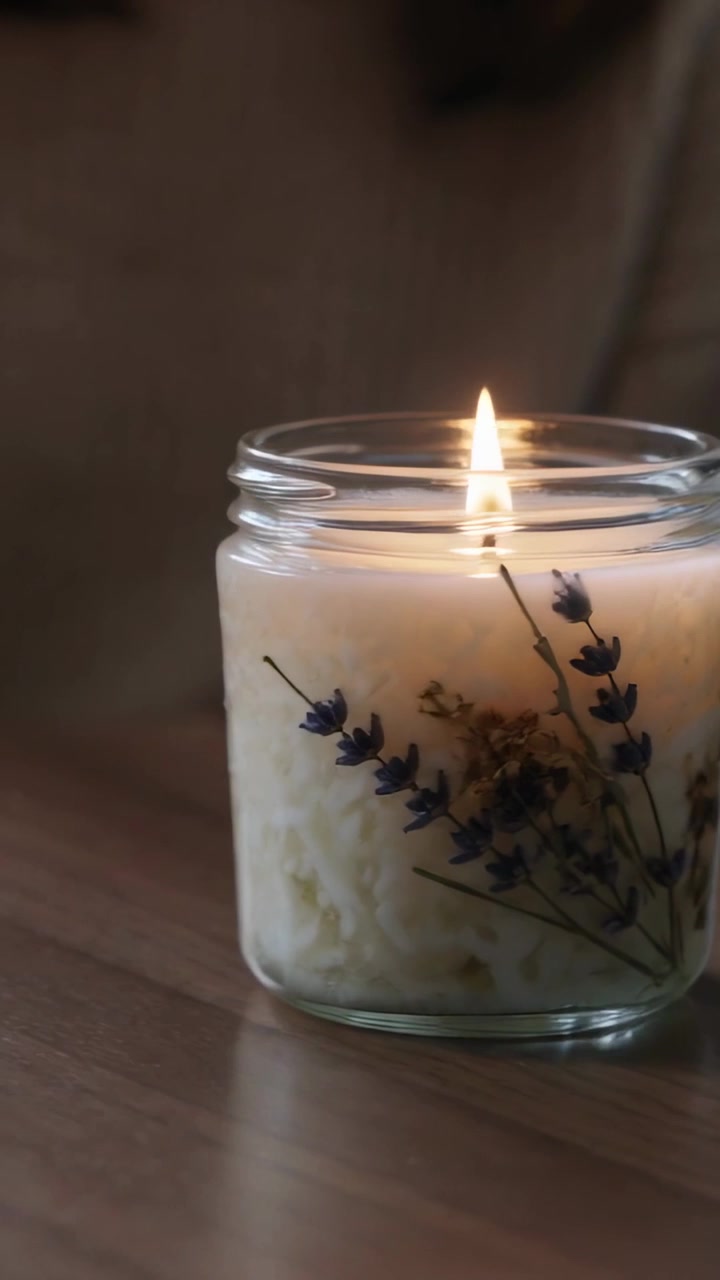 Vertikal video: Hånd i ribbestrikket mansjett tenner et glasslys med en tent fyrstikk hjemme med lavendel, tekstplass.
