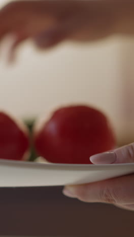 lady puts juicy cucumber to tomatoes on white square plate above table on blurred background in kitchen extreme close view slow motion