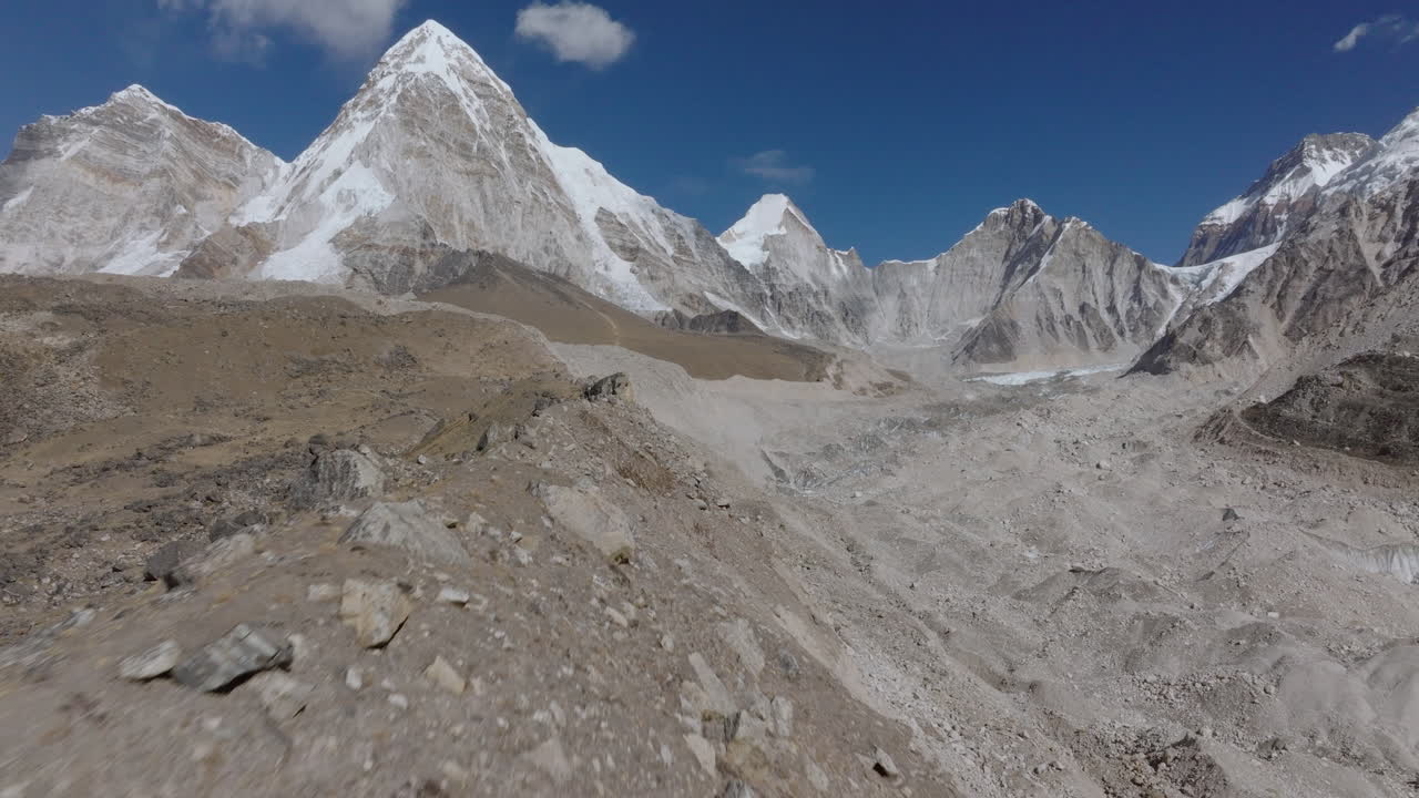 Ripresa aerea con drone che segue una cresta montuosa arida e il ghiacciaio del Khumbu prima di avvicinarsi al picco innevato del Pumori nella regione dell'Everest in Nepal, rivelando un drammatico terreno himalayano.
