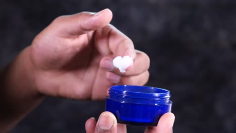 aplicando crema con los dedos de un frasco azul