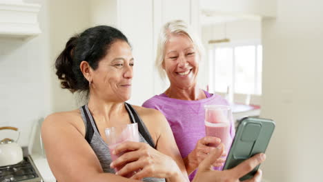 Two-happy-diverse-senior-women-with-cocktails-doing-selfie-in-kitchen,-slow-motion