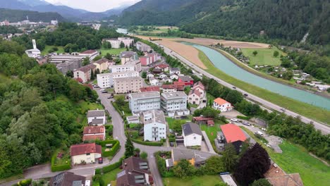 traffic on main street of swiss town. green rhine river in valley of large alps mountains. aerial top down. multi family apartment blocks in suburbia. summer season. wide shot