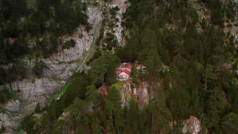 un dron gira lentamente alrededor de una cabaña de piedra rodeada de árboles en un acantilado bajo la cima de una montaña
