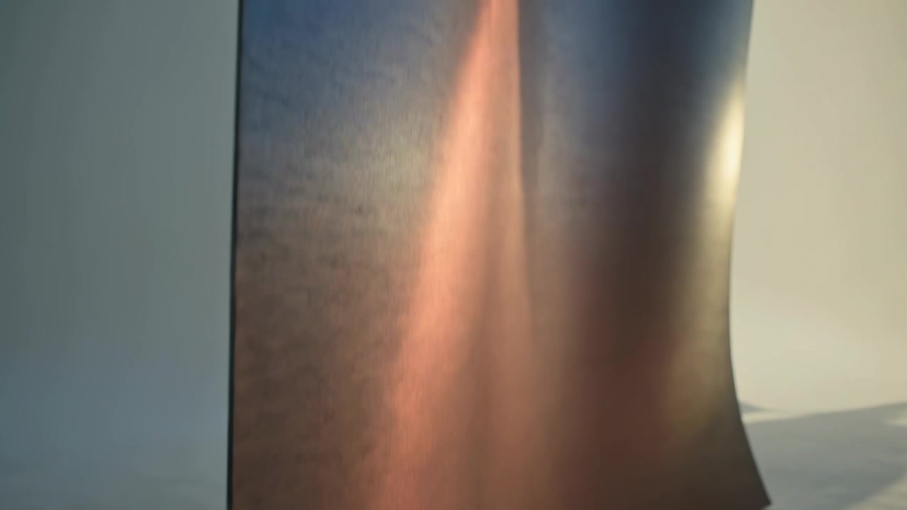 Mostrando um grande painel flexível e reflexivo dobrando e mudando de posição em estúdio, com uma plataforma branca arredondada.