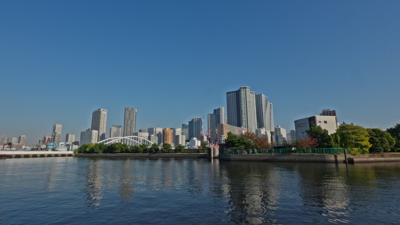 A tranquil Japanese garden features a reflective pond with a traditional wooden bridge, surrounded by lush green trees. Sunlight illuminates the foliage.