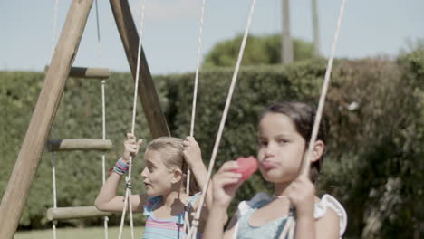 girls in swimsuits swinging on play set while having a snack.