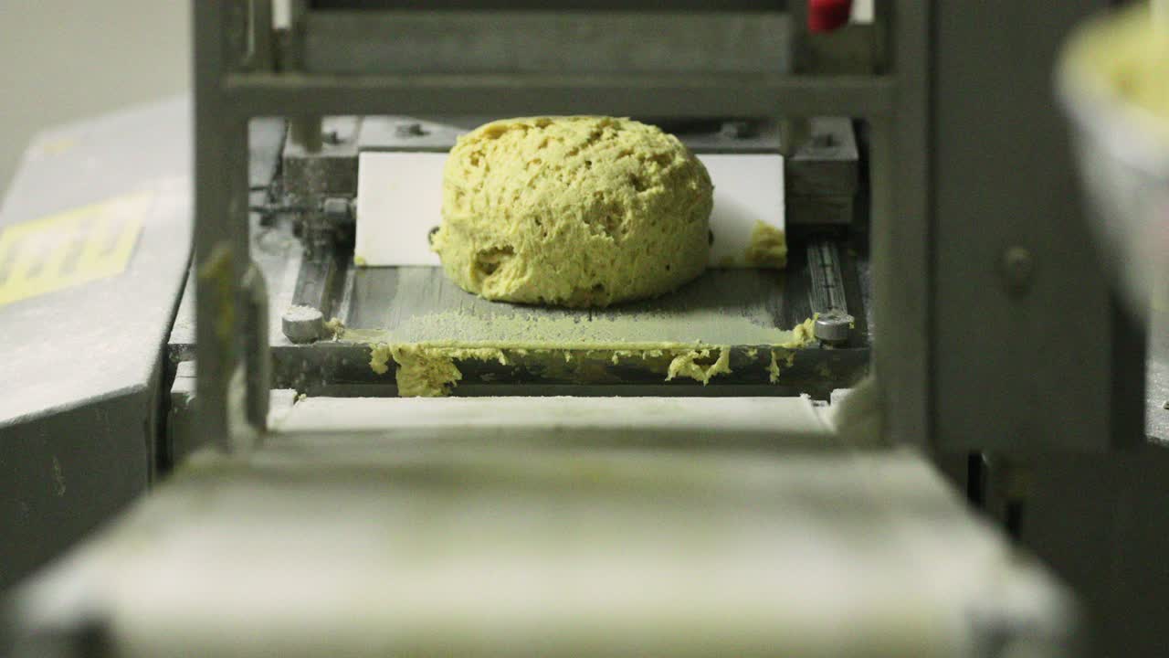 hacer pan en la panadería - la mano del panadero tomando la masa raw amarilla redondeada del equipo de rodadura de la masa