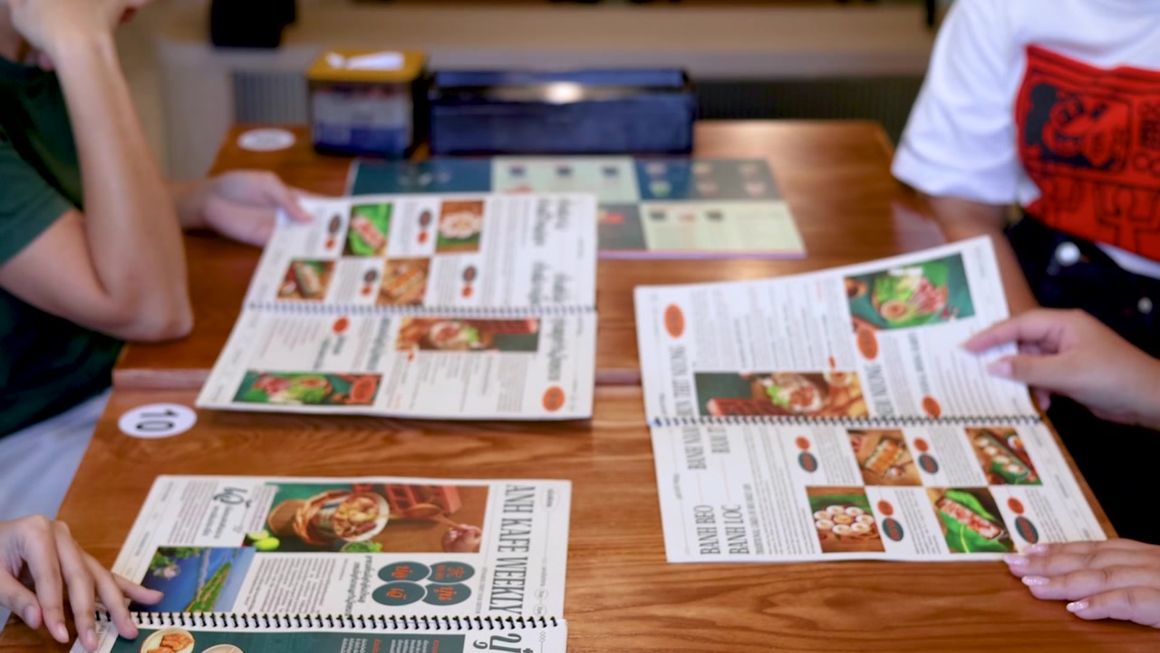 Overhead shot of customers browsing menus at a wooden table in a Vietnamese restaurant