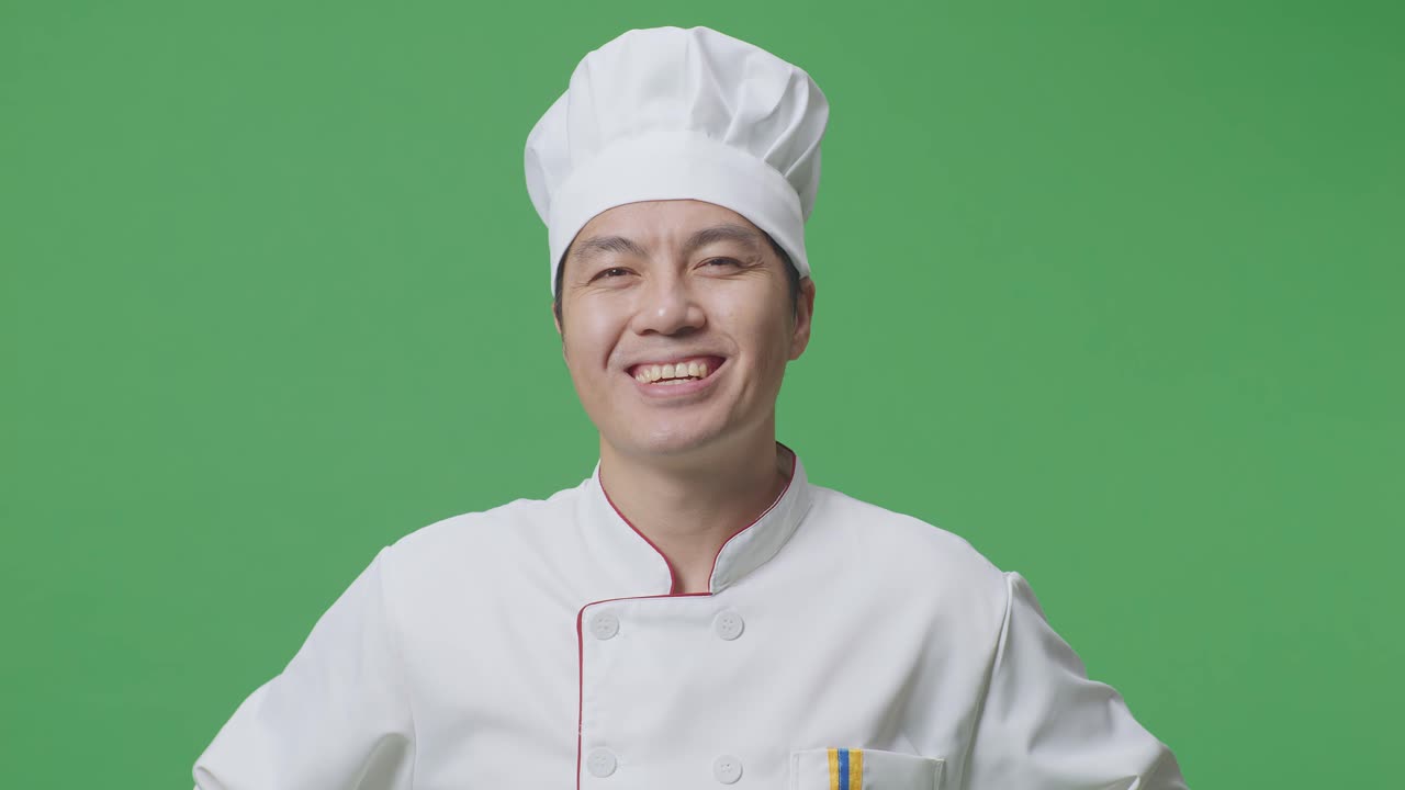 Close Up Of Asian Man Chef With Arms Akimbo Looking At Camera And Smiling While Standing In The Green Screen Background Studio