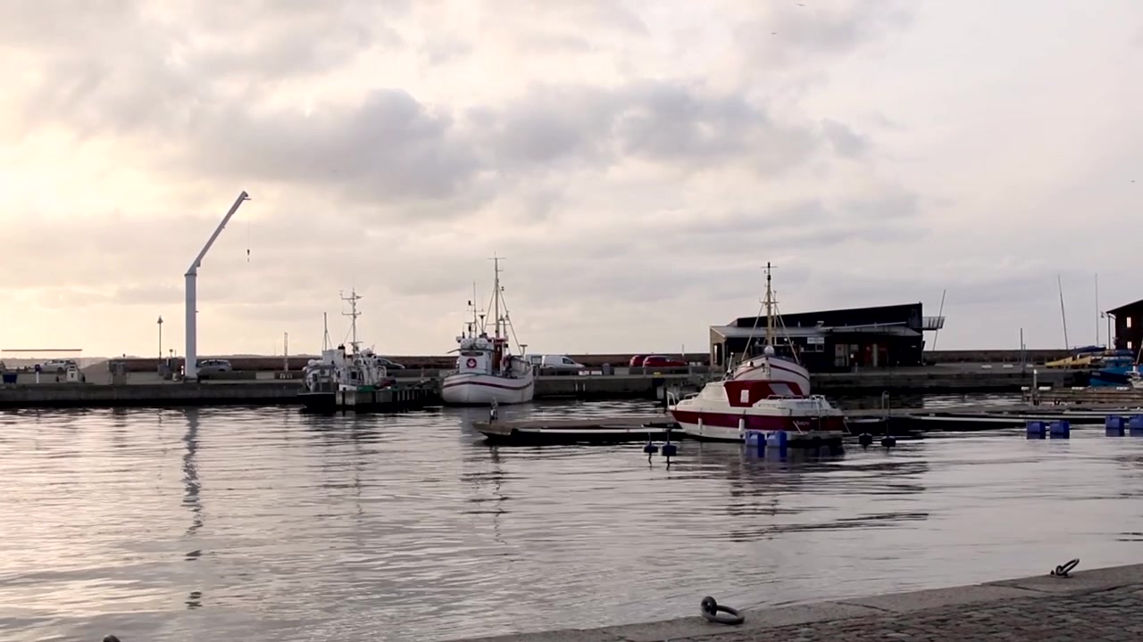 Noen båter flyter rolig på vannet i havnen mens solen går ned bak noen skyer