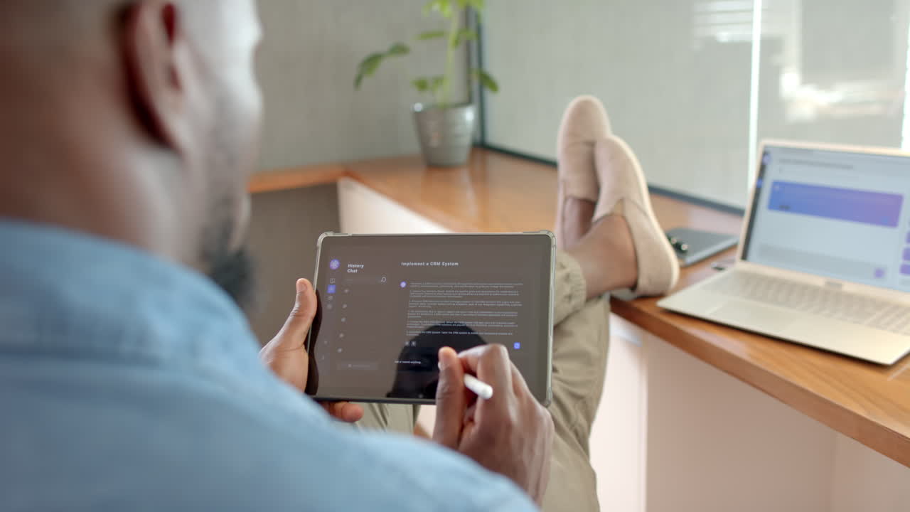 Using stylus on tablet, African American man relaxing with feet up at home