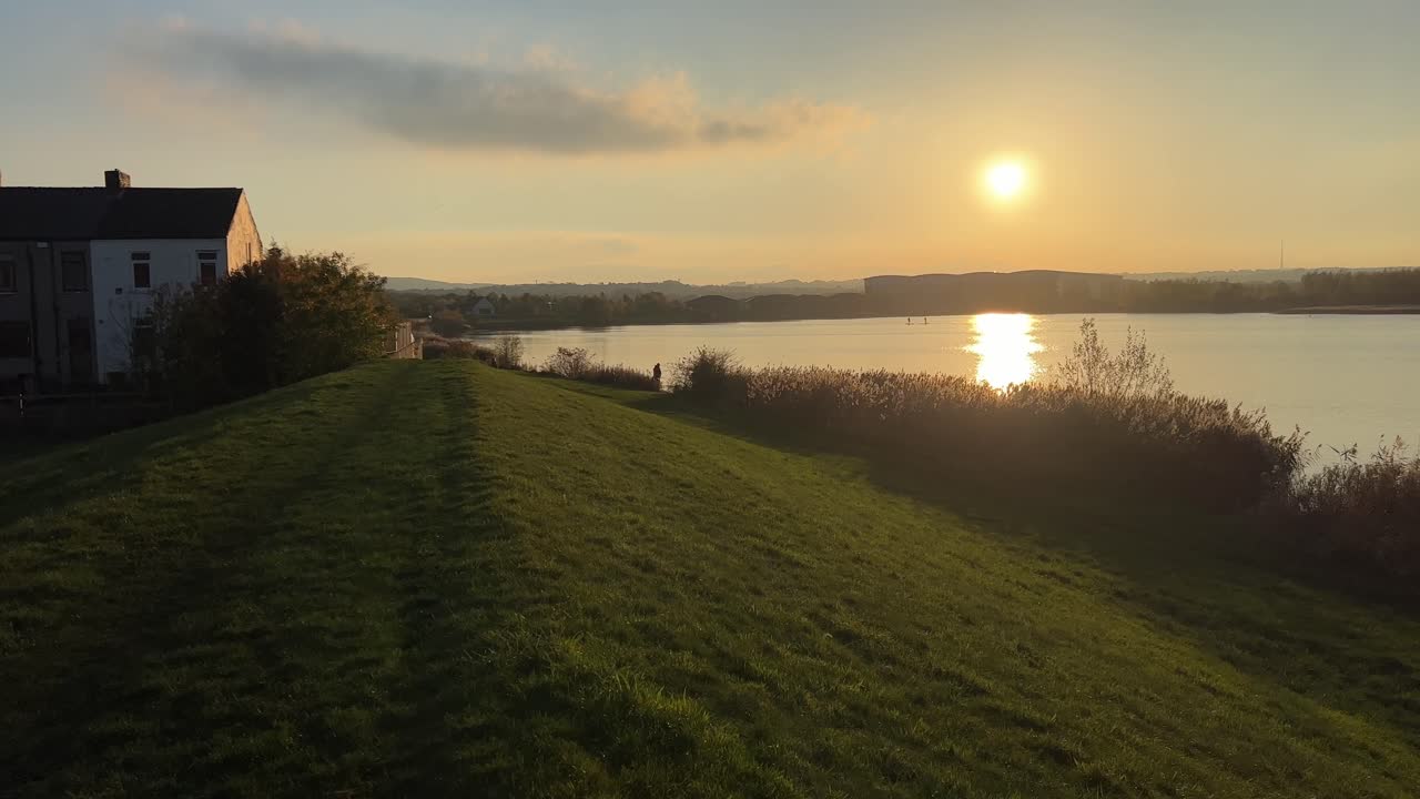 Landlig solnedgangsscene med sø, et rækkehus og gyldne farver
