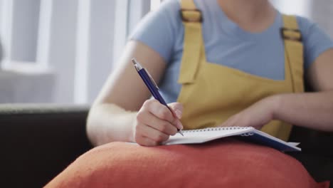 happy biracial woman taking notes and sitting on couch in slow motion