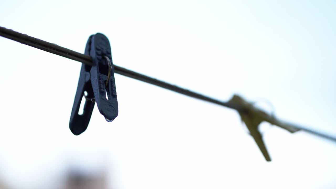 Close-up of a clothespin hanging on a wire against a bright, clear sky