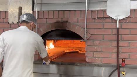 el chef prepara un pan de pizza en un horno de ladrillo local tradicional. calienta la zona caliente. habilidad de cocina. gire la pizza margarita vegetal. comida italiana con queso y pepperoni.