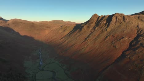 Deep shadowed valley and mountains catching early morning wintry dawn light. Slow panning shot. Langdales, English Lake District, Cumbria, UK.