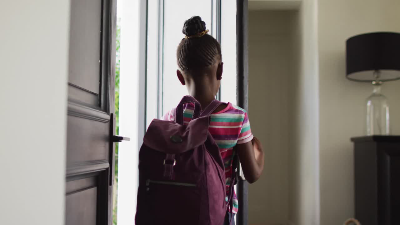 Video of happy african american girl with schoolbag opening front door and leaving home for school