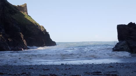 waves crashing onto a sandy beach with castle ruins in the background