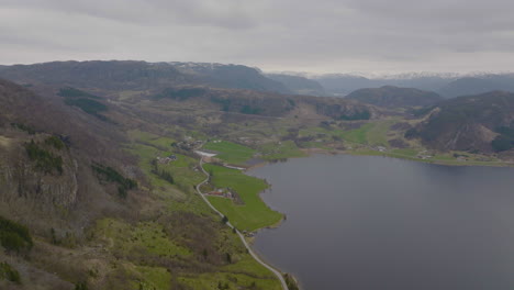 small town and farmland at the end of a lake in a norwegian valley, mountain ranges in the background