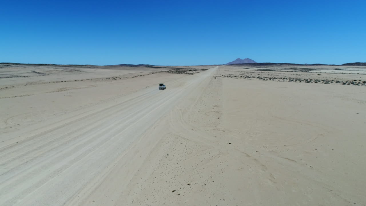 Aerial of the desert in Namibia with a AWD Jeep driving through it and on the background Spitzkoppe.