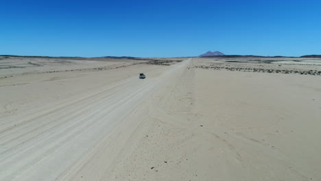 aerial of the desert in namibia with a awd jeep driving through it and on the background spitzkoppe.