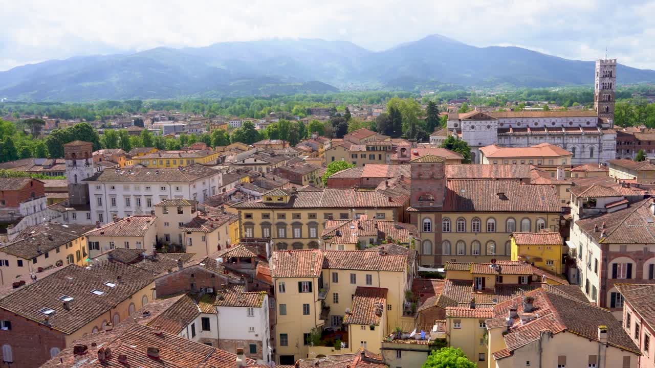 4K panning shot over Lucca, Italy from the top of the clock tower. Scenic view of red rooftops, historic buildings, and Tuscan charm in golden evening light.