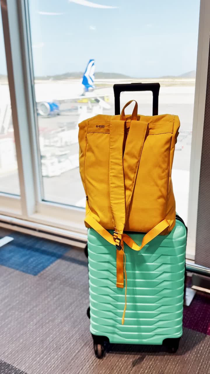 Yellow Backpack and Teal Suitcase by Airport Window View