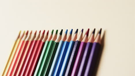 primer plano de lápices de colores dispuestos sobre un fondo beige, en cámara lenta