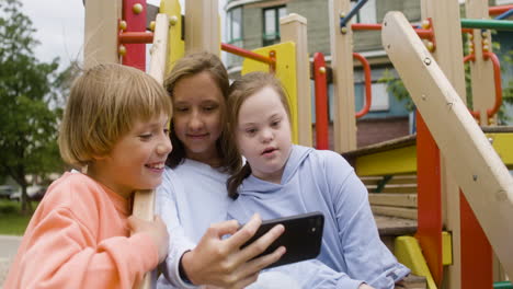 close-up view of a little girl with down syndrome and her friends making a selfie with smartphone in the park on a windy day