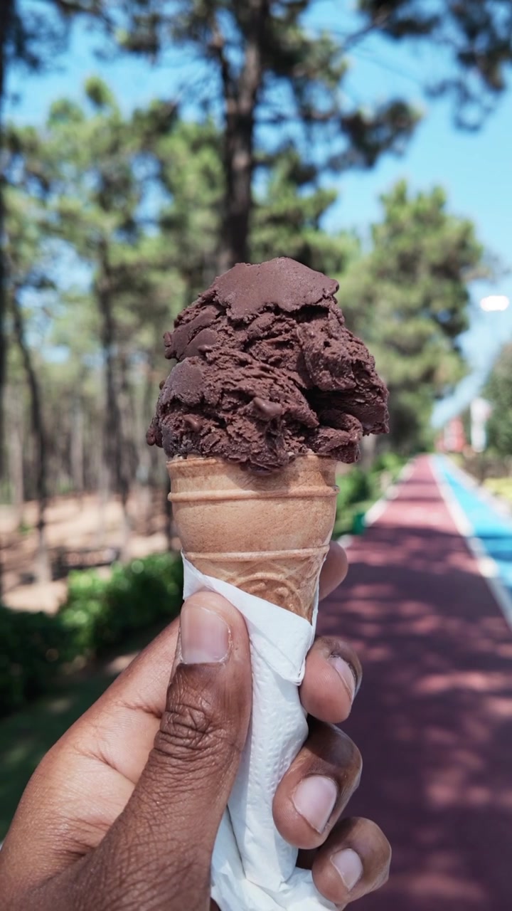 Mano che tiene un cono gelato al cioccolato in un parco