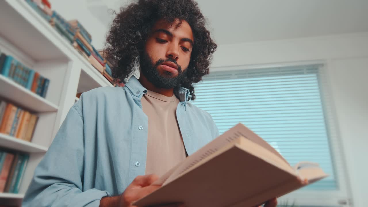 Young carried away arabian man student reading book stands in library